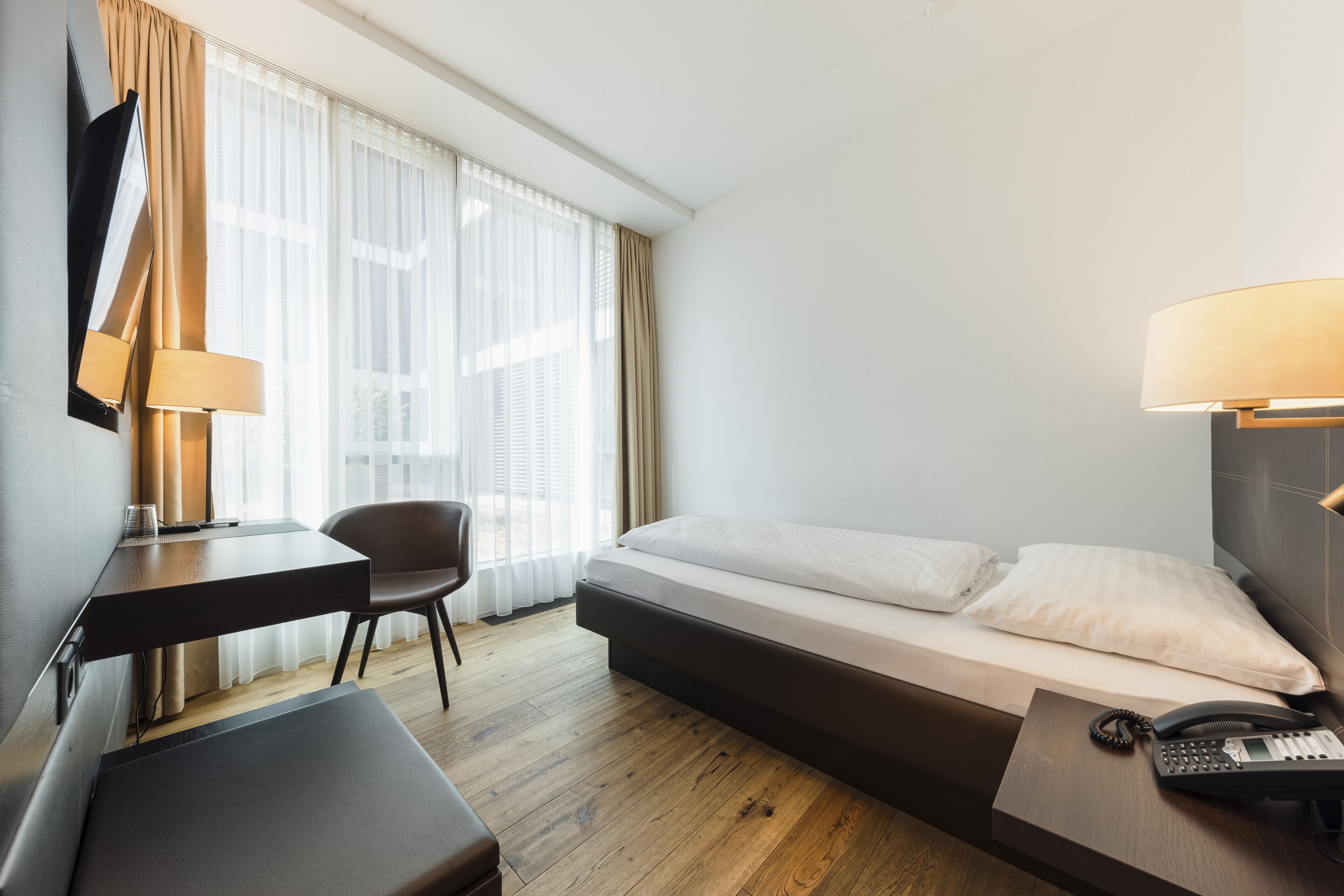 Een hotelkamer met een bed, bureau, stoel, televisie, lamp en telefoon.
