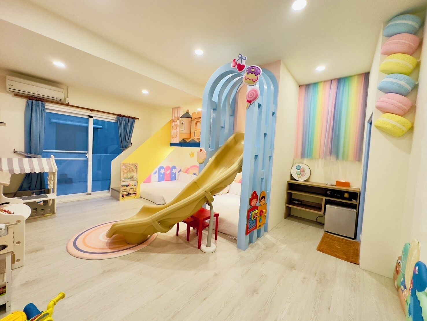 Una sala de juegos infantil con un tobogán, una cocina de juguete y un mural de pared colorido.