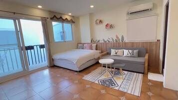 A bedroom with a bed, a sofa, a small table, and a view of the sea through a sliding door.