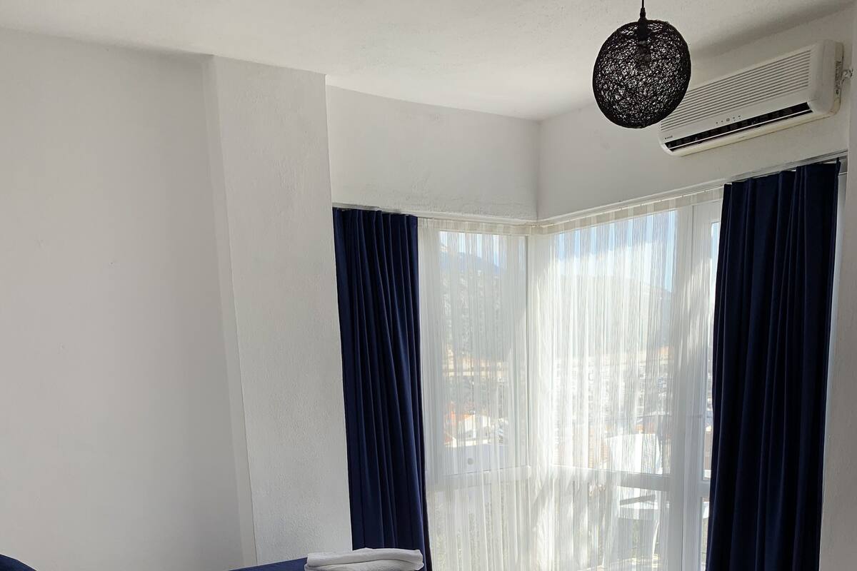 Habitación de hotel con dos camas, ropa de cama blanca, cortinas azul oscuro y una lámpara colgante.