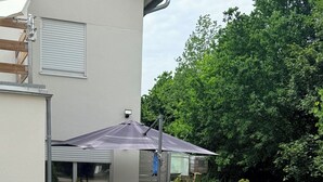 A patio area with a table and chairs, a potted plant, and a large umbrella. - Luxus Ferienapartment “ Im Feldle „ (Kirchheim am Ries)