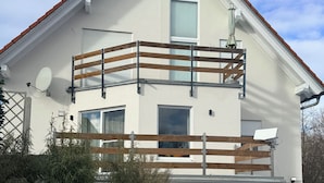 A two-story house with a balcony, a satellite dish, and a stone retaining wall. - Luxus Ferienapartment “ Im Feldle „ (Kirchheim am Ries)