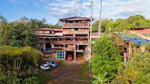 Un bâtiment en bois à plusieurs étages, surmonté d’un toit rouge, entouré d’une végétation luxuriante et s’ouvrant sur un ciel dégagé.