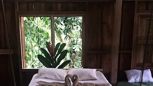 Un lit au design original, une fenêtre donnant sur un paysage verdoyant et un fauteuil suspendu.