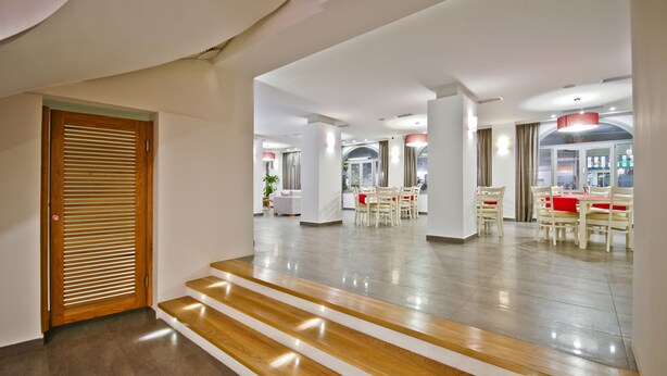 Un interior espacioso con una escalera de madera que lleva a un comedor con sillas blancas y manteles rojos.