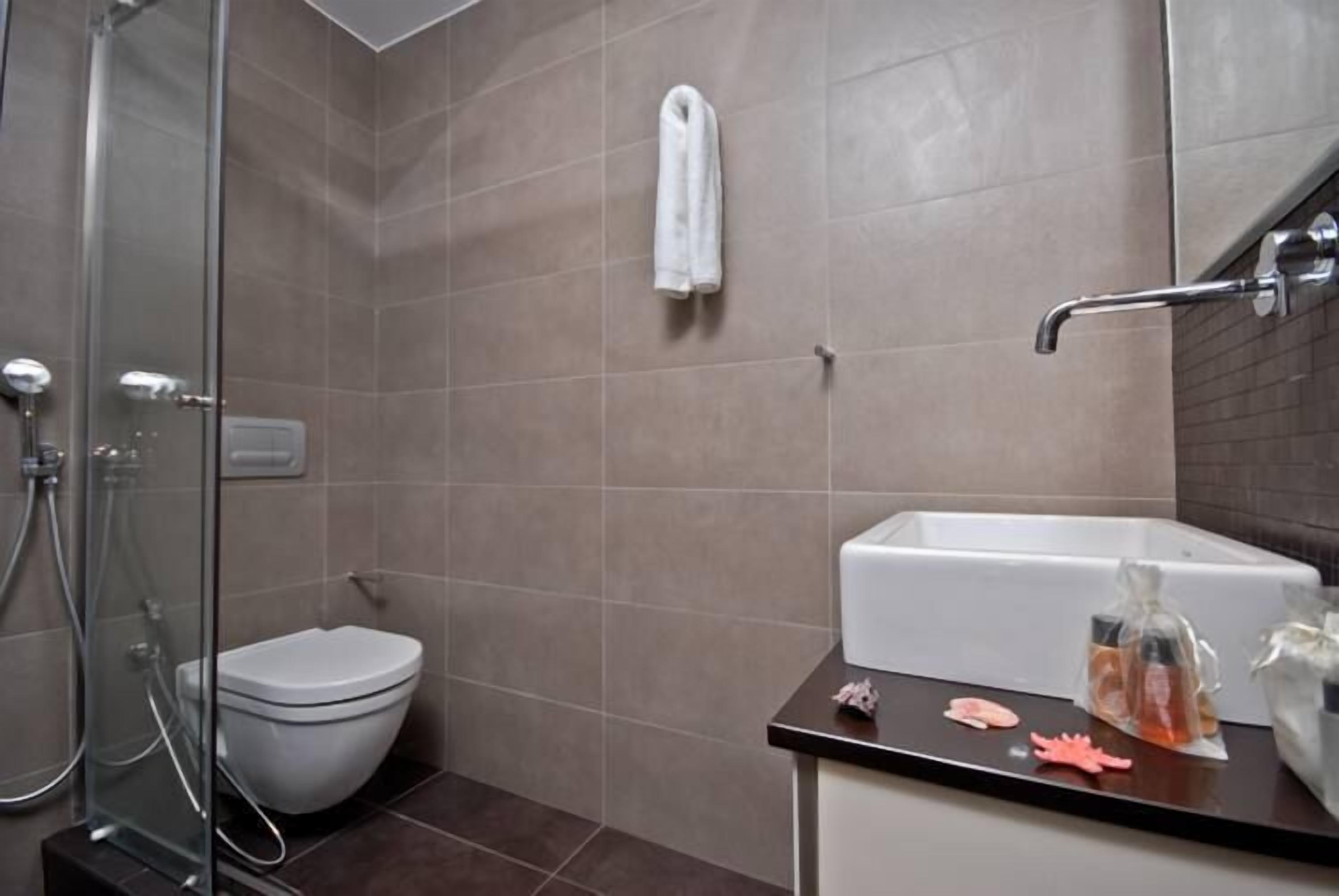 Un baño con cabina de ducha de vidrio, inodoro blanco y lavamanos con artículos de aseo.