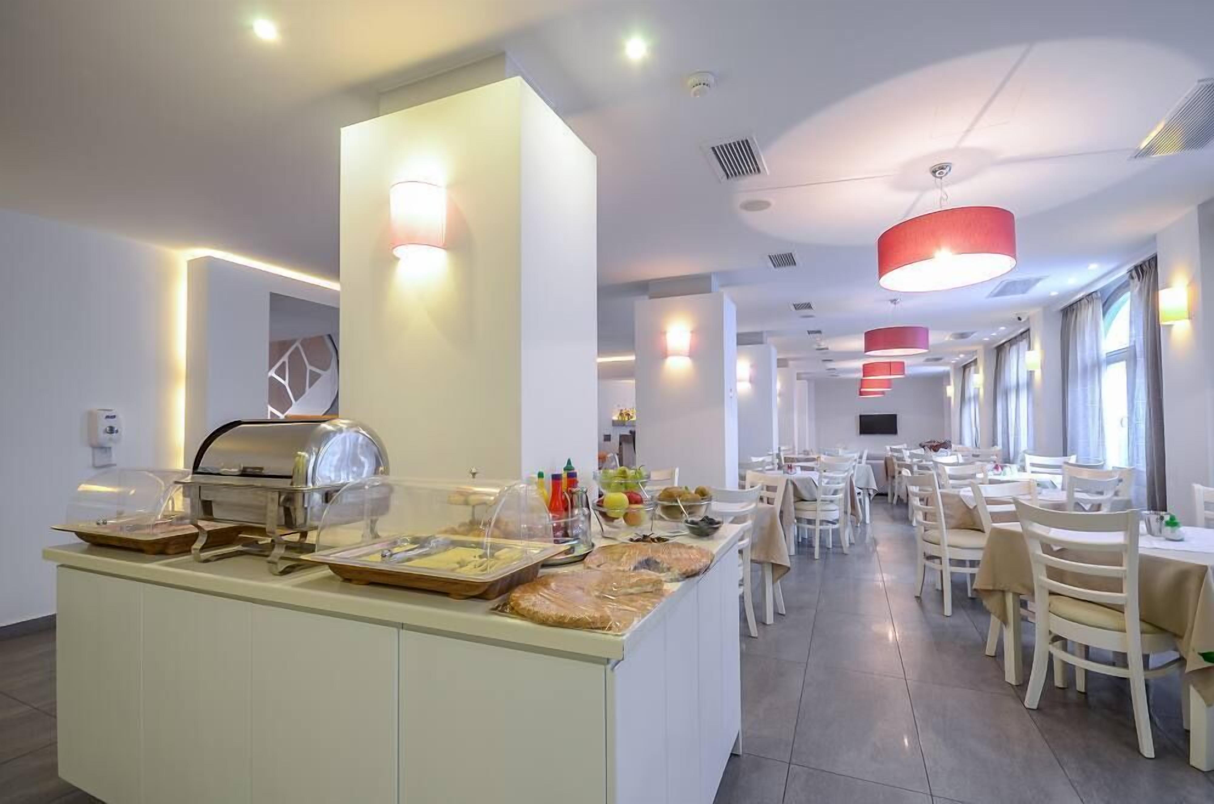 A modern hotel dining area with a buffet setup, multiple dining tables, and pendant lighting.