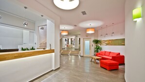 Un área de recepción moderna con un mostrador de madera, un sofá rojo y una escalera que sube a otro nivel.