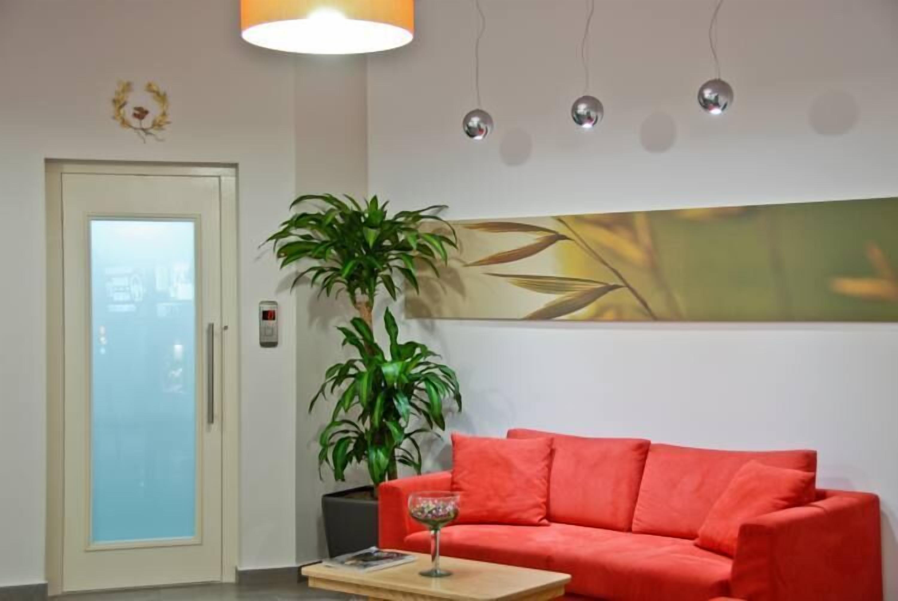 A room with a red sofa, a potted plant, a glass table with a drink, and a door with frosted glass panels.