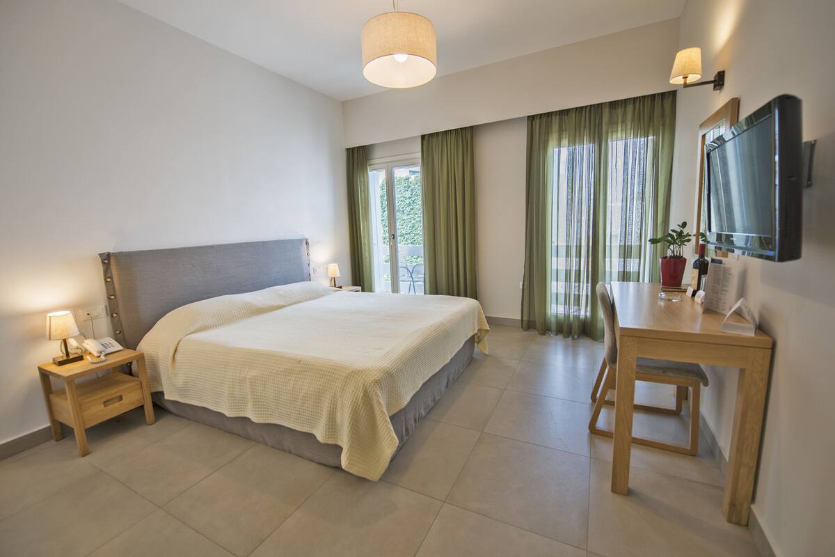 A bedroom with a bed, bedside table, lamp, and a desk with a chair.