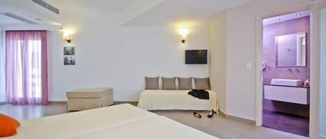 A hotel room with two beds, a sitting area, a television, and a bathroom with a mirror and sink.