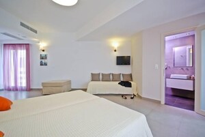 Habitación de hotel con dos camas, una zona de estar, televisión y baño con espejo y lavamanos.