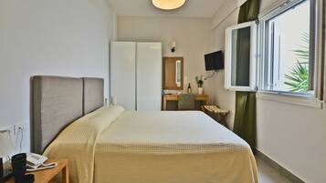 A hotel room with a bed, a desk with a telephone, a mirror, a television, and a window with curtains.