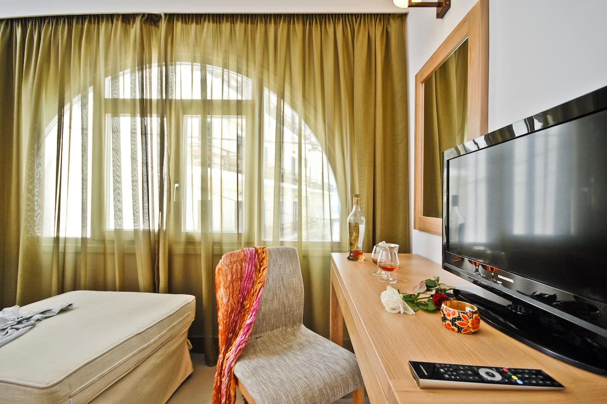 A hotel room with a bed, a TV, a desk with a remote control, and a window with curtains.