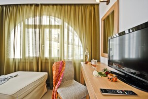 Habitación de hotel con cama, televisión, escritorio con control remoto y ventana con cortinas.