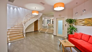 Un moderno vestíbulo de hotel con una escalera espiral, un sofá rojo, una mesa de centro de madera y una planta en maceta.