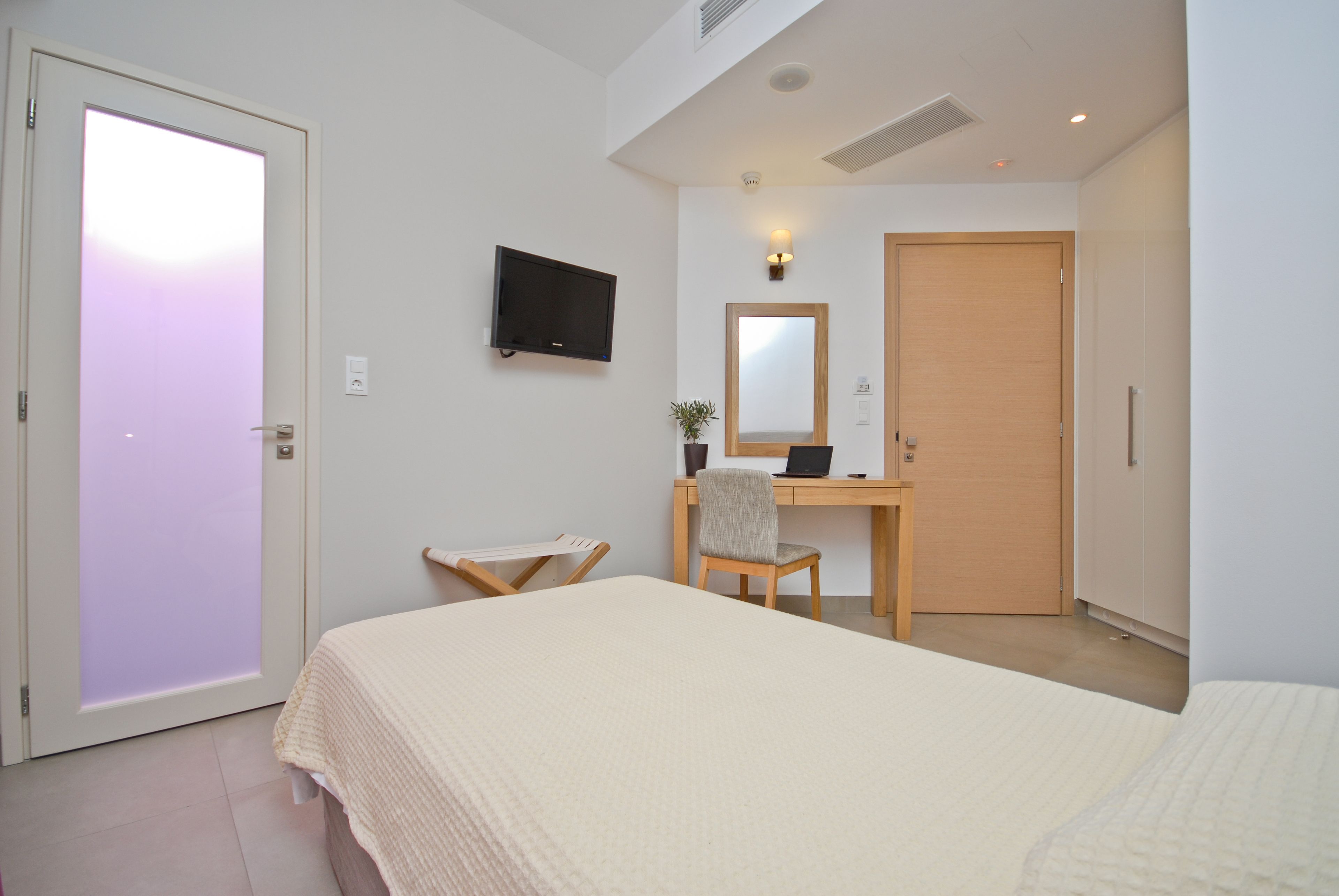 A bedroom with a bed, a desk with a chair, a television, and a wardrobe.
