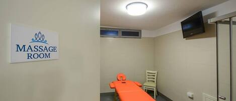 A massage room with a massage table, a chair, a TV mounted on the wall, and a sign indicating the room's purpose.