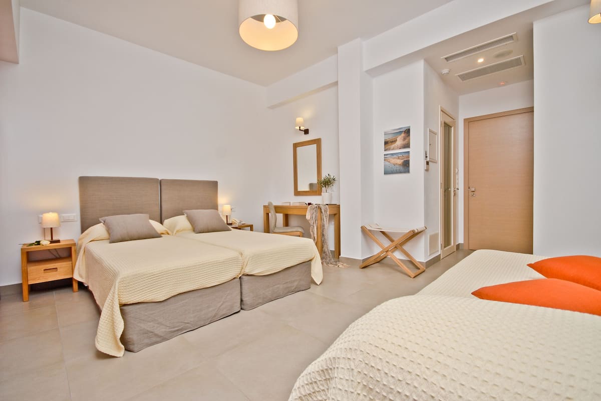 A modern hotel room with two beds, a desk, a chair, and a wardrobe.