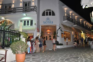 Un hotel llamado 'Xenia' con fachada blanca, un balcón y una entrada acogedora.