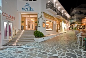 Un hotel llamado 'Xenia' con un acceso empedrado, una escalera que conduce a la entrada y un letrero que dice 'COLOURS' a la izquierda.