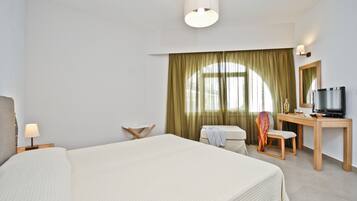 Una camera d'albergo con un letto grande, una scrivania con televisore, una sedia, una lampada e una finestra con tende.
