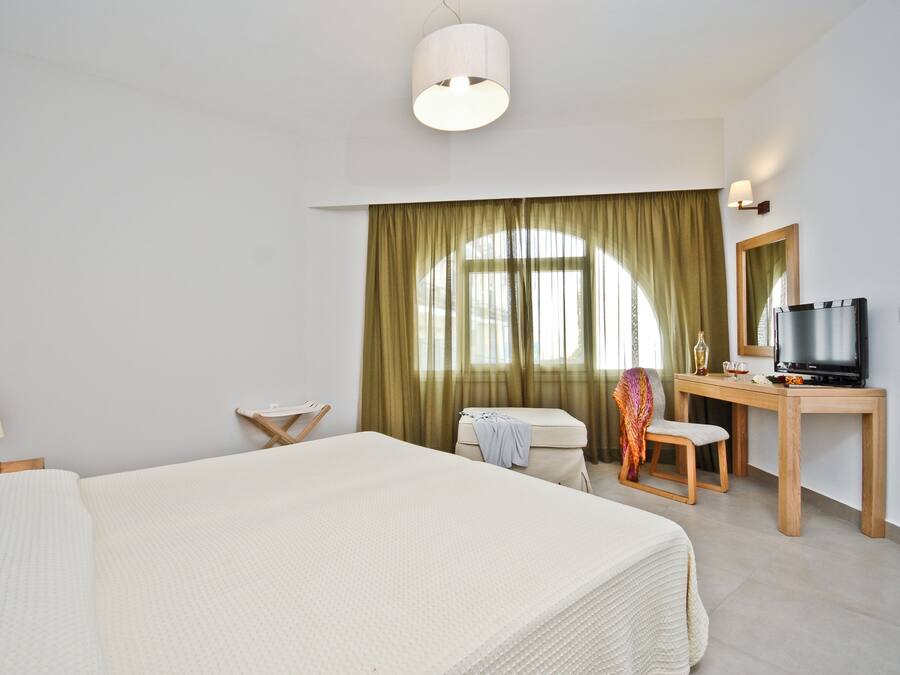 A hotel room with a large bed, a desk with a TV, a chair, a lamp, and a window with curtains.