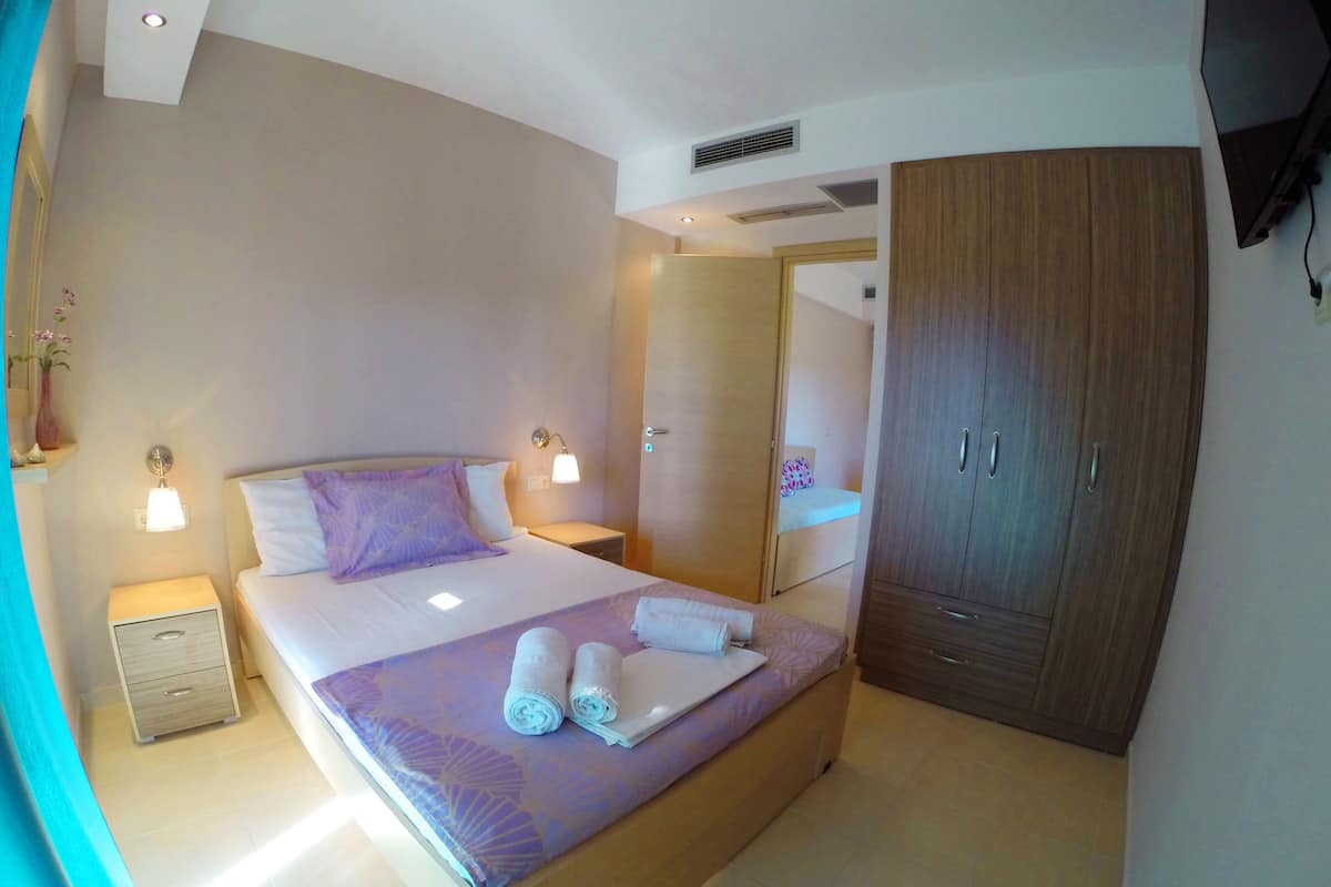 Hotellihuone, jossa on suuri sänky, vaatekaappi, yöpöytä ja seinälle asennettu televisio.