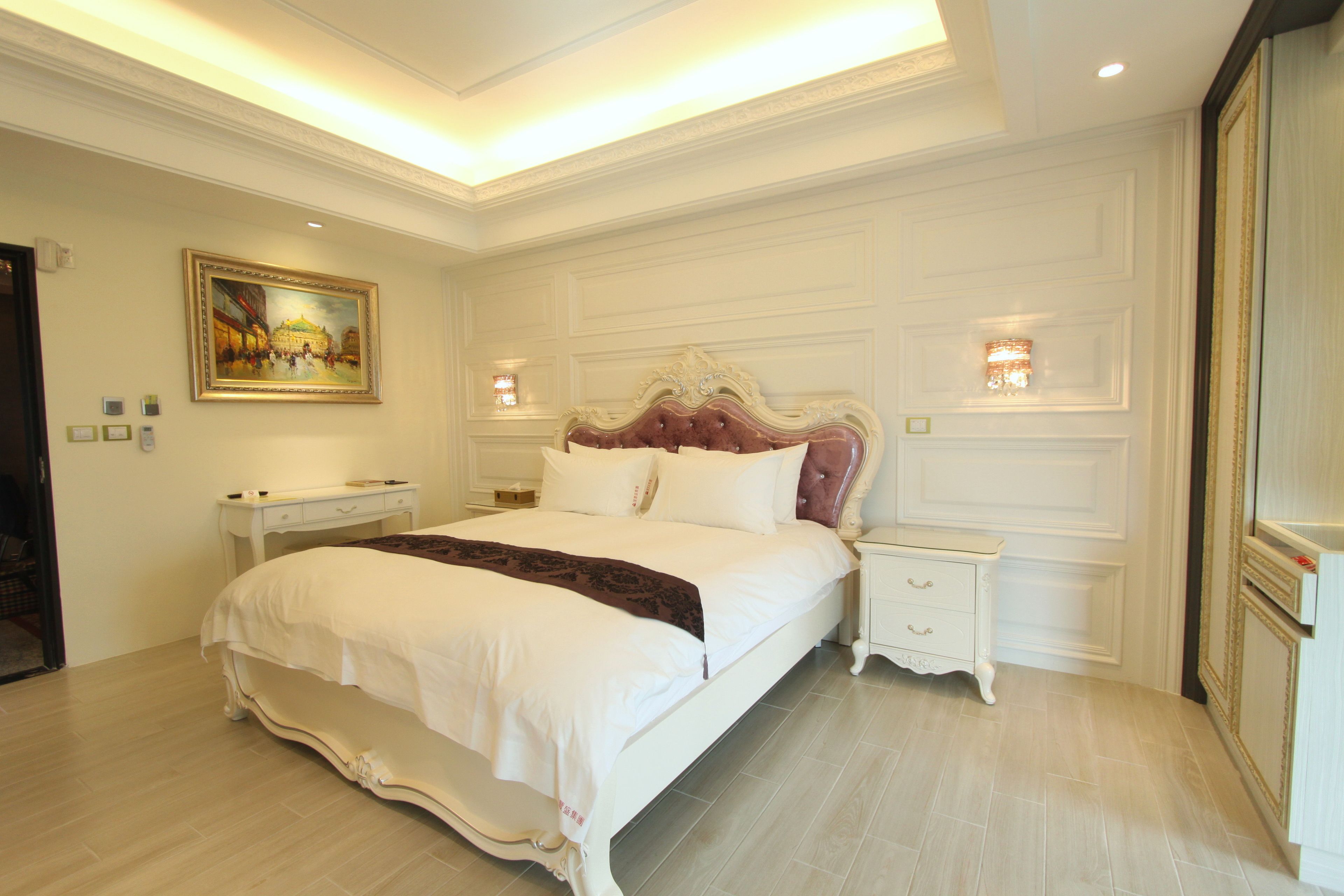A spacious bedroom with a large bed, a nightstand, a dresser, and a painting on the wall.