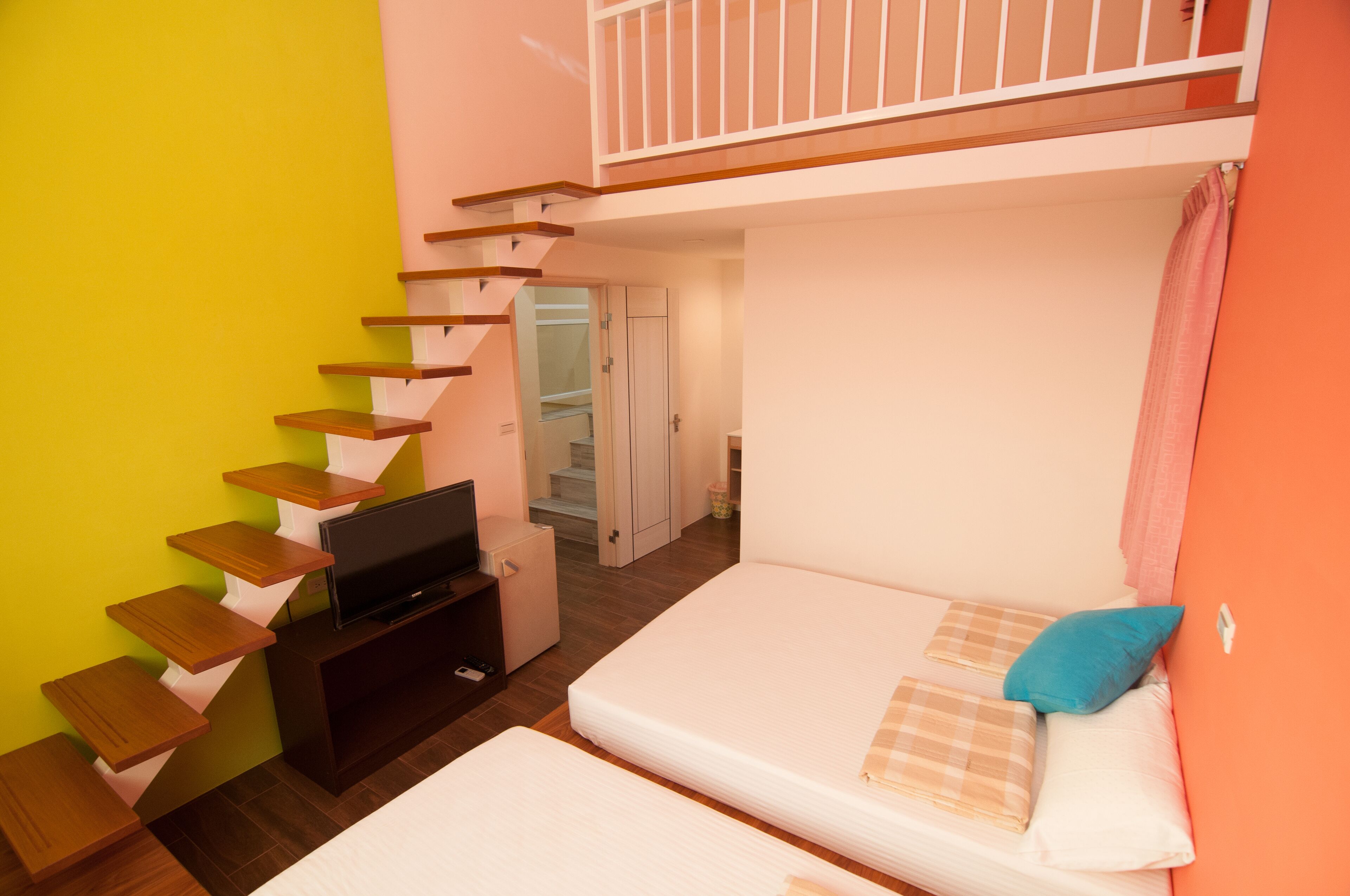 Una habitación pequeña con una cama, un televisor sobre un soporte de madera y una escalera que sube a un nivel superior.