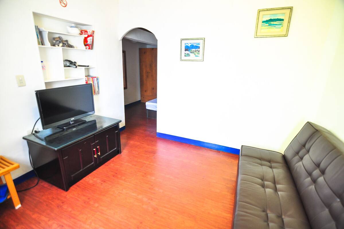 A living room with a TV on a cabinet, a sofa, and a hallway leading to another room.