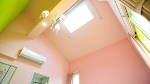 A room with a pink wall, a ceiling fan, an air conditioning unit, and a window with curtains.