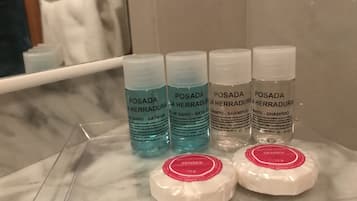 Une étagère de salle de bain avec des bouteilles de shampoing et de gel douche de la marque Posada La Herradura, ainsi que deux savons.