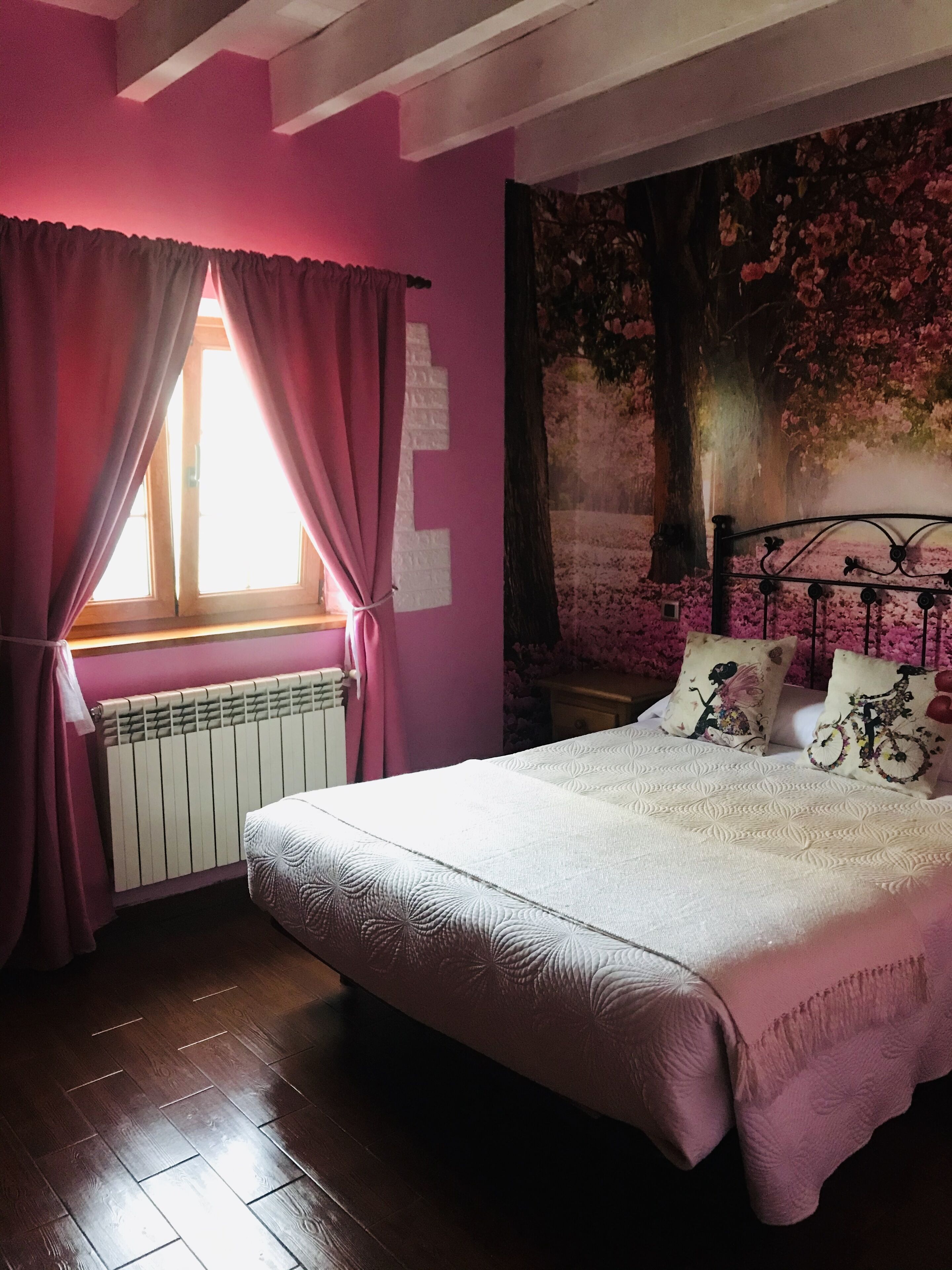 Un dormitorio con cama, ventana con cortinas, radiador y un tapiz en la pared.