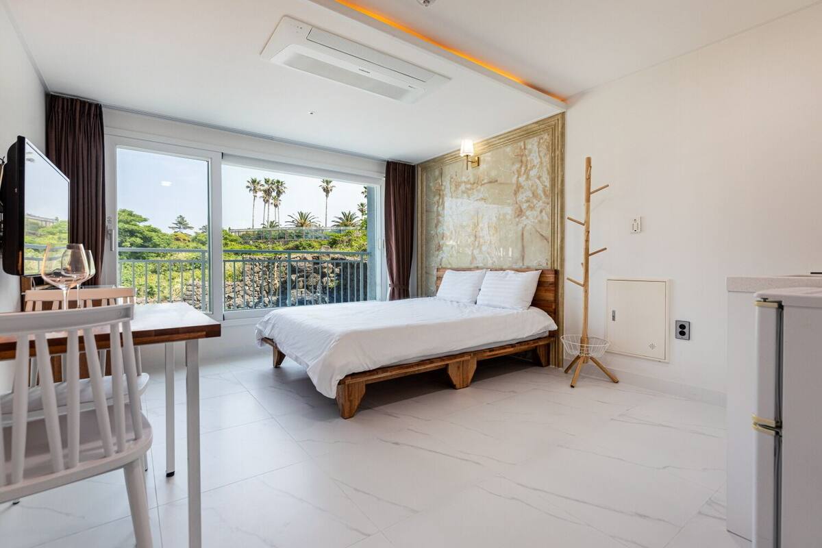 Une chambre d’hôtel moderne dotée d’un grand lit, d’un coin repas et d’un balcon offrant une vue sur les palmiers.