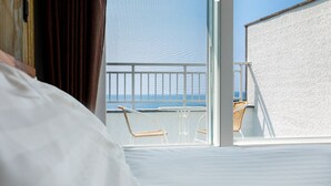 A hotel room with a balcony overlooking the sea, featuring a bed, a chair, and a small table. -  Aewol Oceanstay (Jeju City)