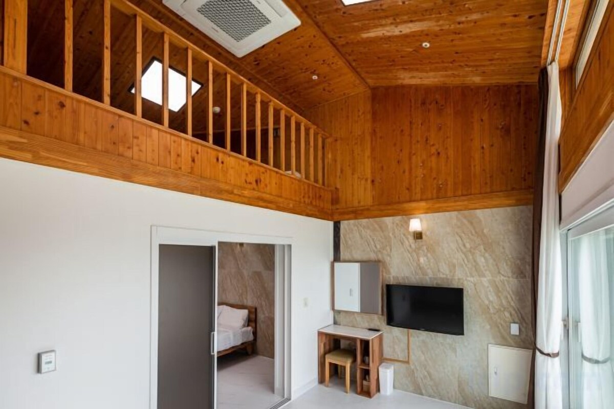 Una habitación con techo de madera, una cama, un escritorio y un televisor.