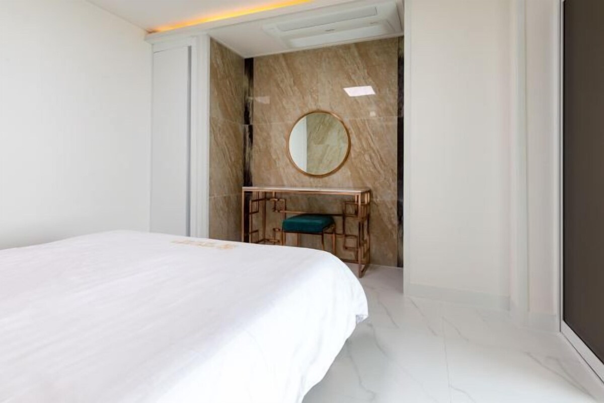 Une chambre d’hôtel avec un grand lit, une coiffeuse en bois avec un miroir et un mur en marbre.