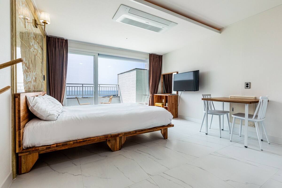 Une chambre avec un lit en bois, un bureau avec une chaise, une télévision et un balcon avec vue.