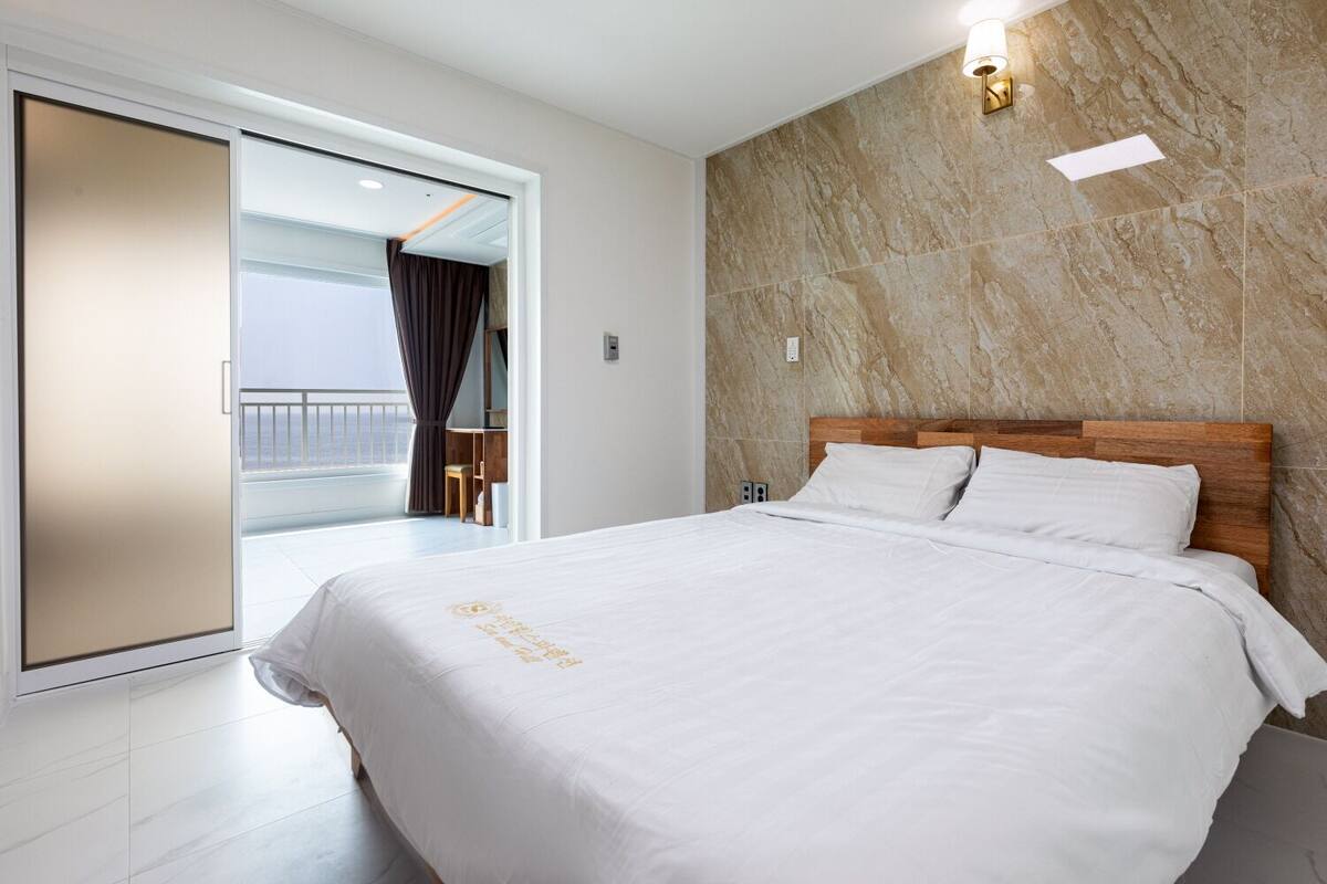 Une chambre d’hôtel avec un grand lit, une tête de lit en bois et une vue sur la mer, accessible par une porte coulissante.