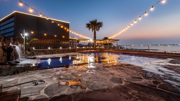 A pool area with a waterfall, string lights, and a modern building with large windows. -  Aewol Oceanstay (Jeju City)