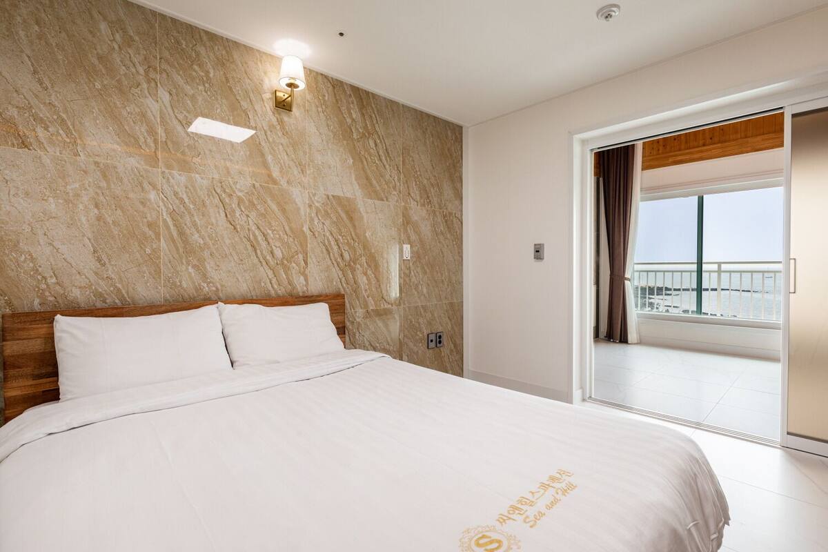 Une chambre d’hôtel avec un mur en marbre, un lit avec du linge de maison blanc et un balcon offrant une vue sur la mer.