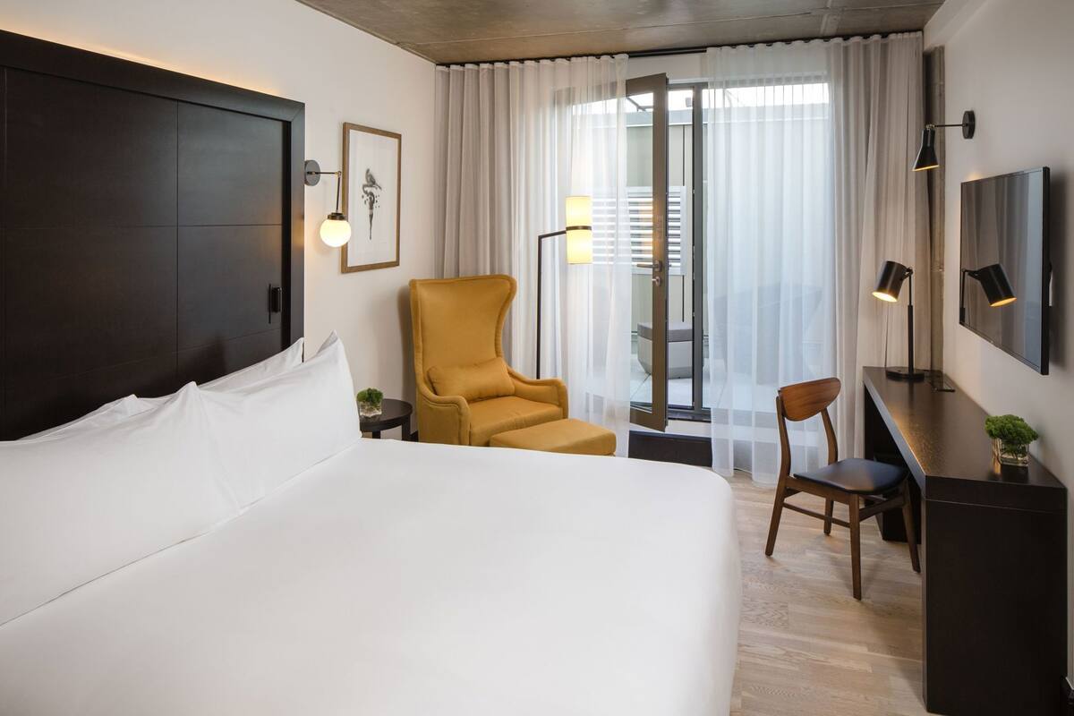 Une chambre d’hôtel avec un grand lit, un bureau, une chaise, une télévision et une fenêtre avec des rideaux.