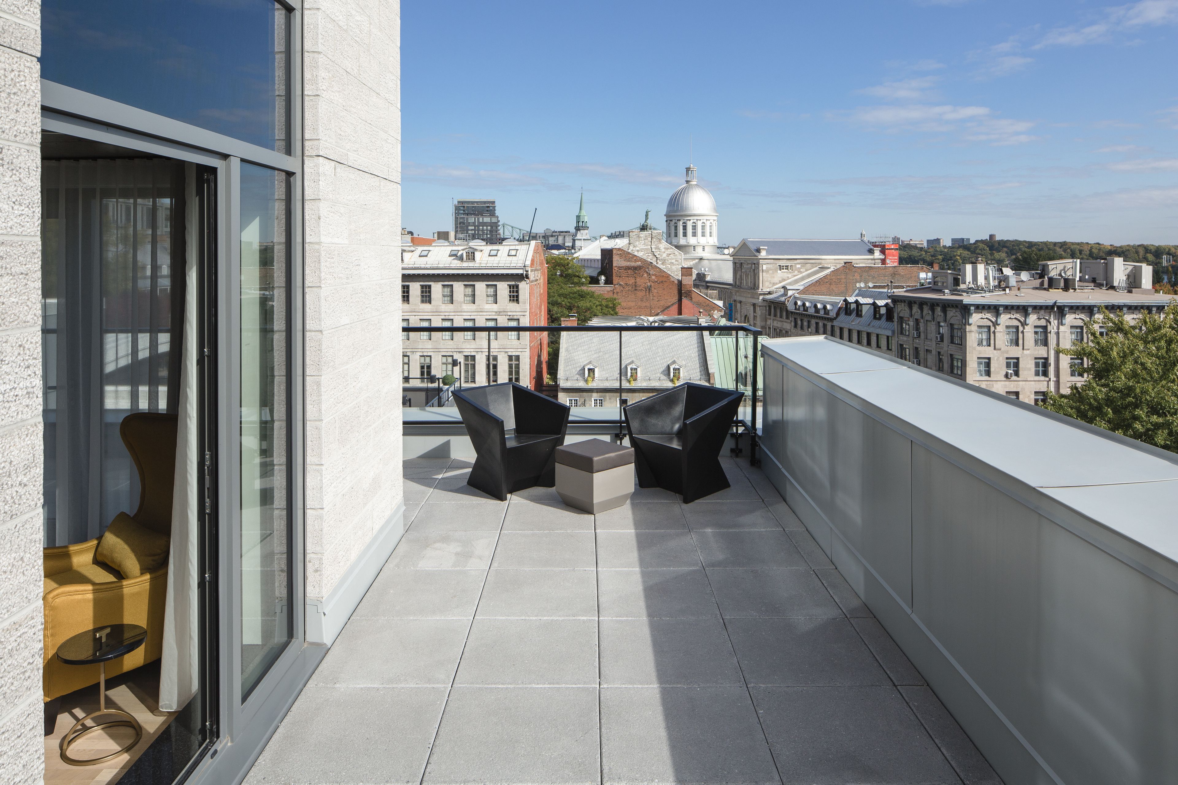 A balcony with two black chairs and a small table, overlooking a cityscape with historic buildings and a dome structure.