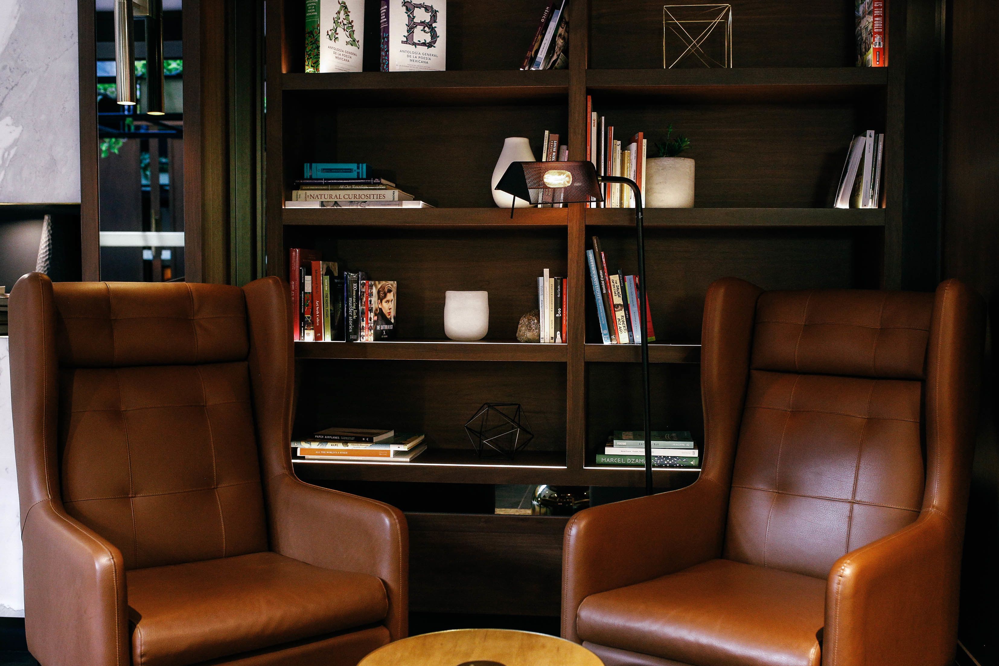 A room with two leather armchairs, a wooden coffee table, and a bookshelf filled with books and decorative items.