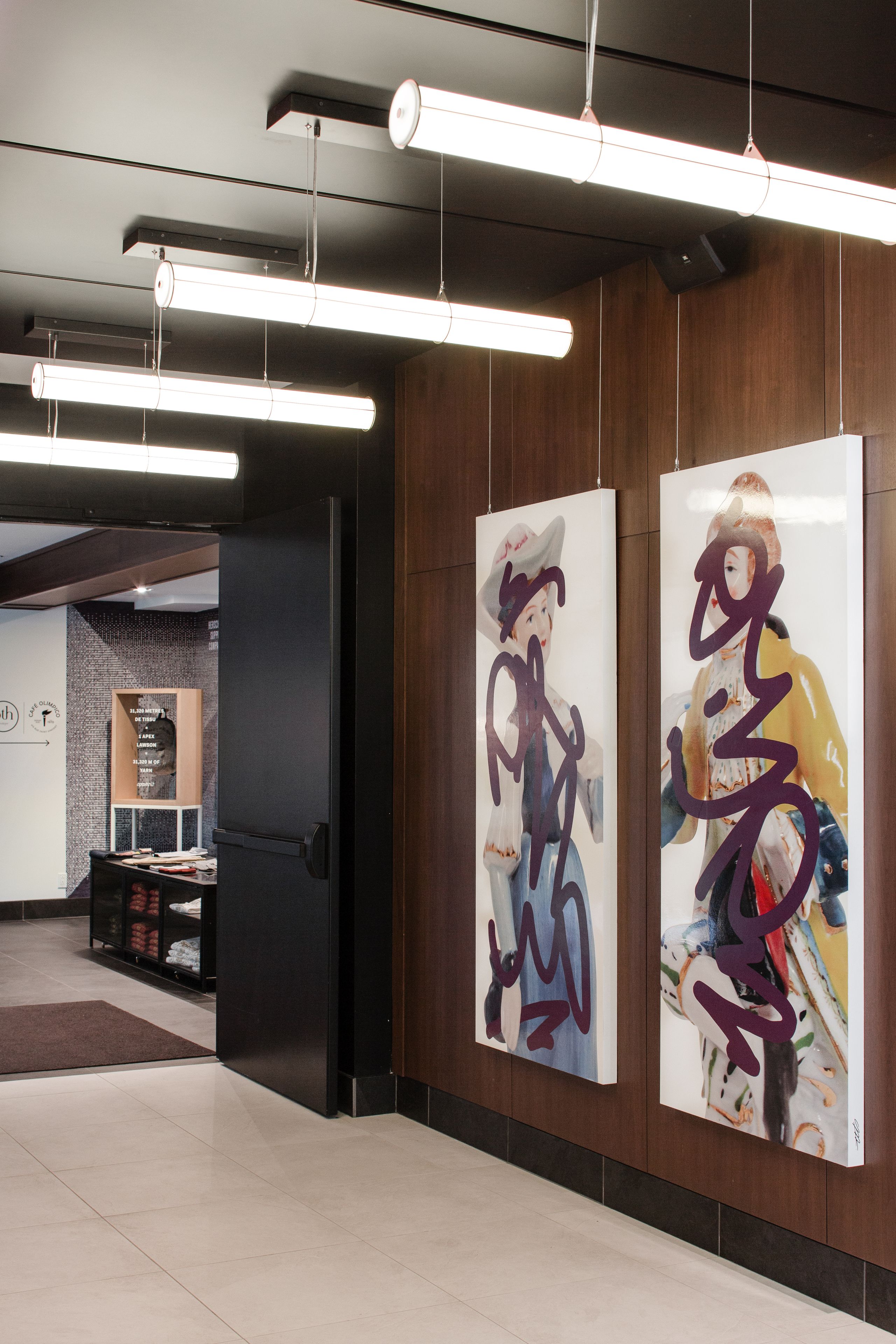 Um interior moderno com painéis de madeira, uma porta preta e duas grandes pinturas abstratas.