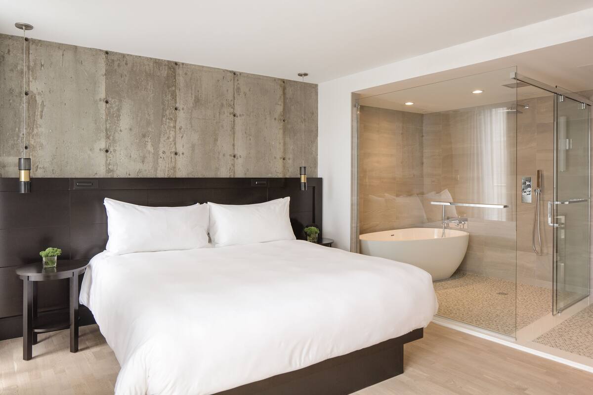 Une chambre d’hôtel moderne dotée d’un grand lit, d’une table de chevet, d’une douche en verre et d’une baignoire.