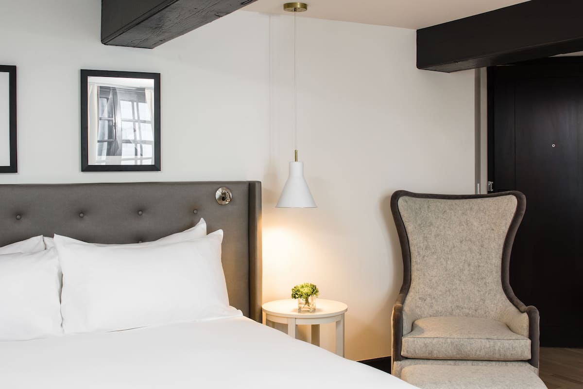 Une chambre bien rangée, avec un lit, une chaise, une table de chevet avec une lampe et des tableaux encadrés accrochés au mur.