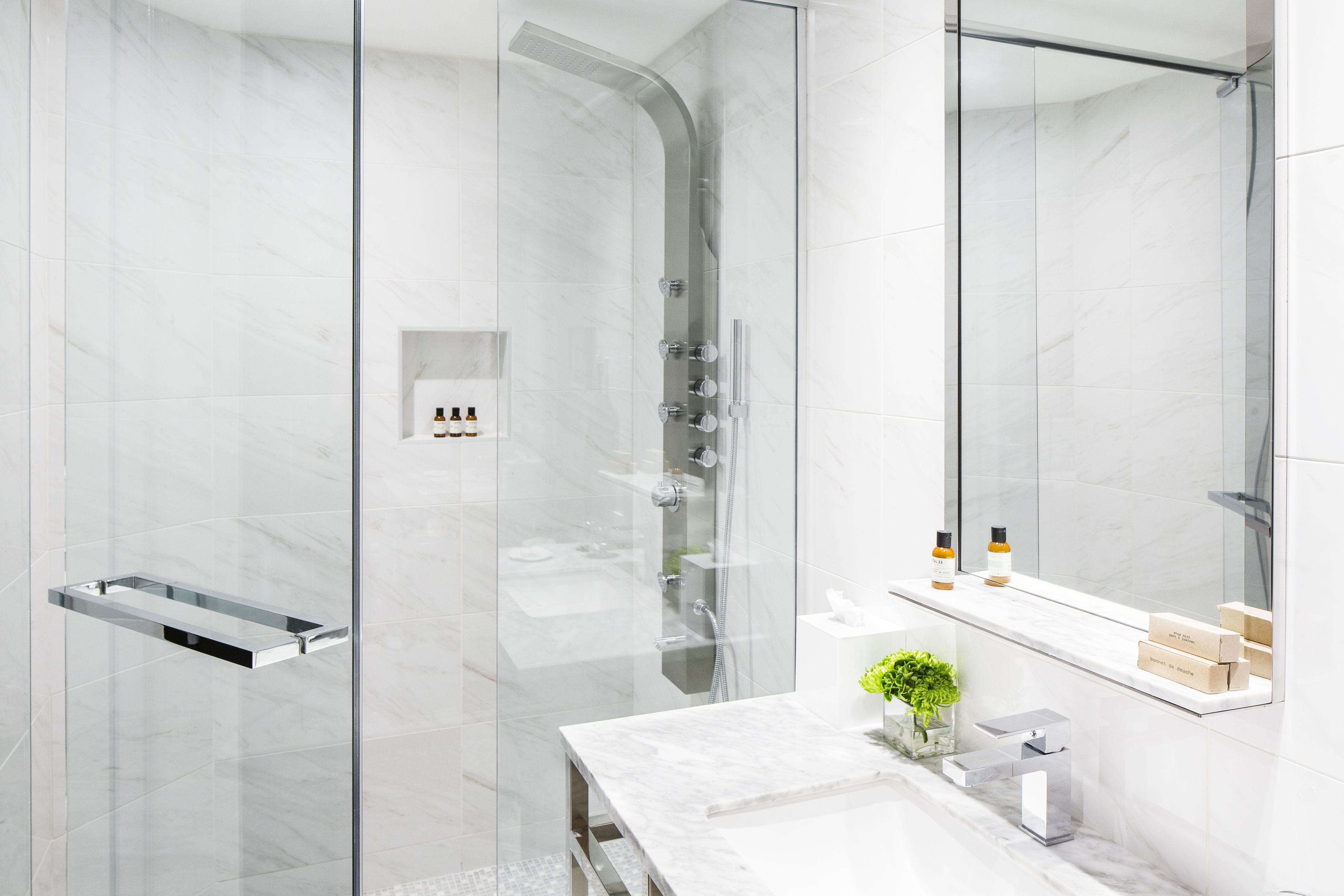 Un baño moderno con cabina de ducha de vidrio, lavamanos de mármol y espejo sobre el lavamanos.