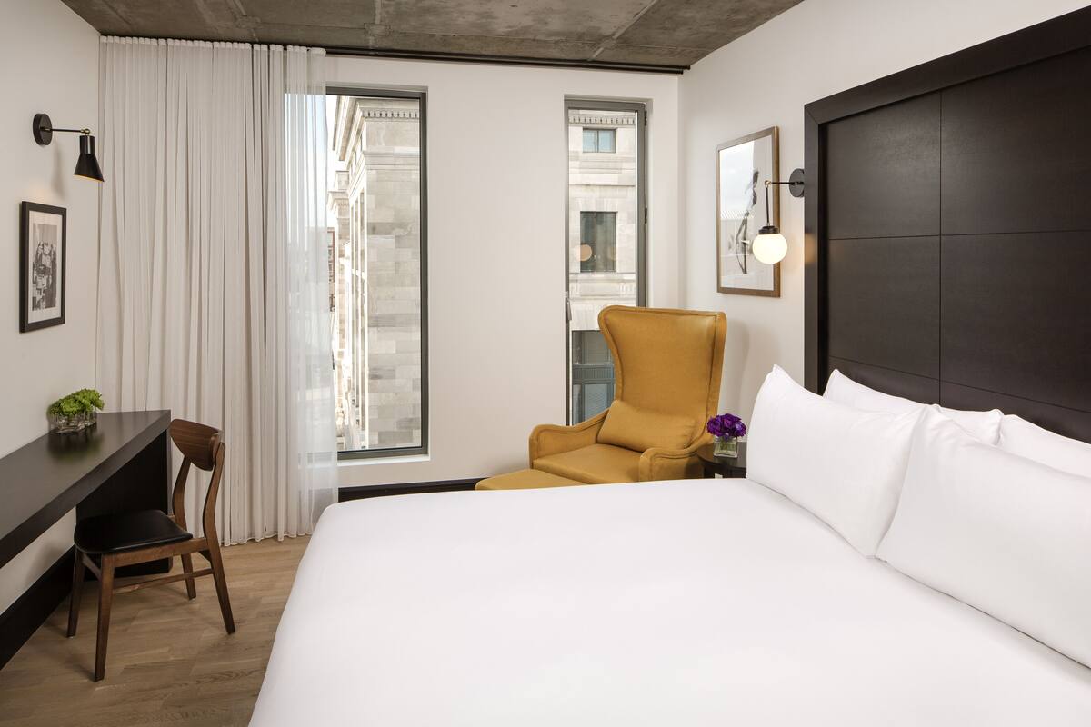 Une chambre d’hôtel avec un grand lit, un bureau, une chaise et une fenêtre avec des rideaux.